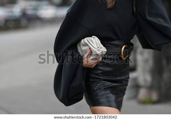Street style outfit – Woman wearing a\
black oversized sweater and leather skirt matched with a clutch bag\
– StreetStyleFW2020