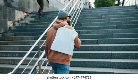Street style portrait of young man wearing brown blank hoodie with white blank textile eco shopping bag or tote bag. Mock up for design - Powered by Shutterstock