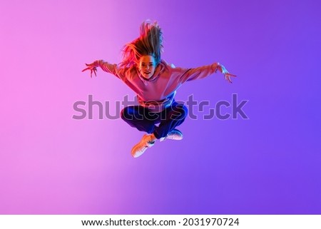 Street style. Young beautiful female hip-hop dancer dancing isolated on neon studio background. Sport achievement, spirit of expression. Concept of dance, youth, hobby, dynamics, movement, action, ad