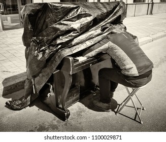 Street of the summer city. On the road is a piano. The piano is covered with a blanket. The man is sleeping on the keys. Photographed in Ukraine, Kiev. Horizontal frame. Black and white image - Powered by Shutterstock