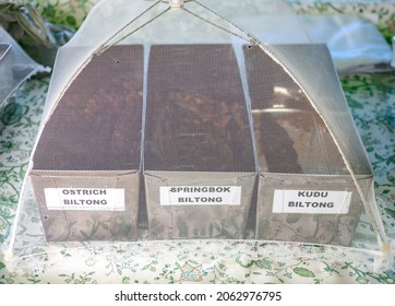 Street Trading Of Ostrich, Springbok And Kudu Meat Biltong At  Village Market In South Africa.  Containers With Dried Meat Of Wild Animals And Birds Are   Traditional Dish Of African Cuisine.