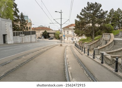 Street with a train track running down the middle. The train tracks are empty. The street is lined with trees and buildings - Powered by Shutterstock