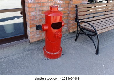 A street urn in the form of a fire hydrant stands next to a bench on the street - Shutterstock ID 2213684899