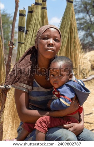 street vendor with the child in the village , young african woman standing in front of a brooms rack in a sunny day on the side of the highway
