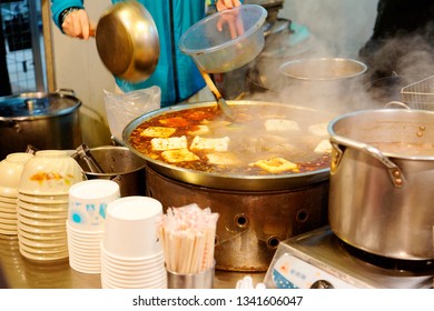 A street vendor cooking spicy stinky tofu (a pungent smelling, fermented tofu & one of Taiwanese people's favorite snacks ) in a steaming pot of hot chilli stock, in a market stall in Taipei, Taiwan   - Shutterstock ID 1341606047