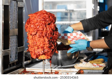 A street vendor, at a street food market, wearing gloves, preparing al pastor meat, at a stand selling Mexican food lunches to customers - Powered by Shutterstock