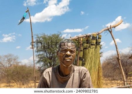 street vendor in the village , african man standing in front of a brooms rack in a sunny day on the side of the highway