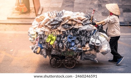 A street vendor wearing a straw hat, pushes a cart overflowing with shoes, navigating through a road at Vietnamese Hanoi Old Quarter on a Vietnam city,