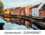 Street view with colorful brick houses near river in the small english town Norwich, England in autumn. Townhouses Buildings At Waterfront. Suburb Houses, Residential Building Near River In Europe.