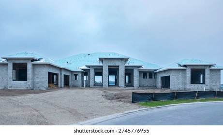 Street view of interconnected oncrete shells of a large, upscale, hurricane-resistant house under construction in a suburban residential development on a cloudy morning in southwest Florida