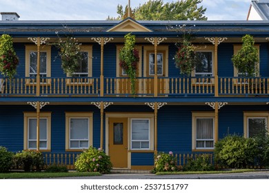 A street view of an old blue wooden building with yellow and white trim. The residential rental has three doors, multiple windows and hanging baskets of flowers. The exterior apartments are Victorian. - Powered by Shutterstock