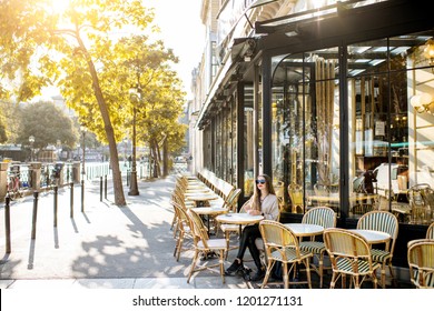 Street view on the traditional french cafe with young woman sitting outdoors during the morning light in Paris