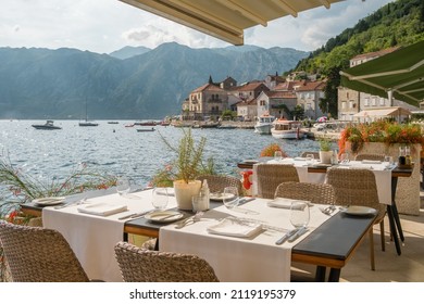 Street view of a outdoor waterfront terrace with tables and chairs in restaurant in Perast historic village in Kotor Bay, Montenegro. Summer vacation destination concept