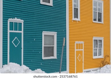 A street view of two wooden adjoined houses. The yellow exterior wood building has multiple glass double hung windows with white trim. Both have wooden storm doors. There's drifts of fresh white snow. - Powered by Shutterstock