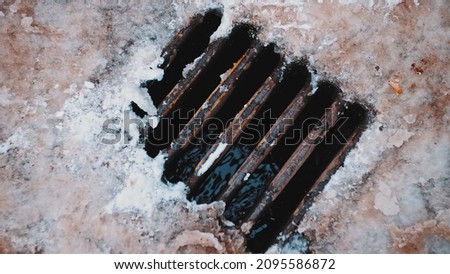Street Water Drain Sewer with Rusty Grating Collecting Water from Thaw Melting Snow and Ice on Winter Day