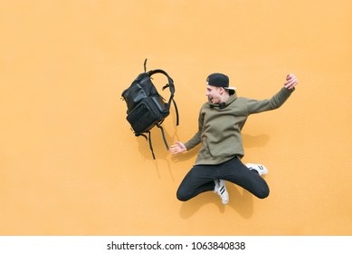 Street young man jumping with a backpack on the background of an orange wall - Shutterstock ID 1063840838