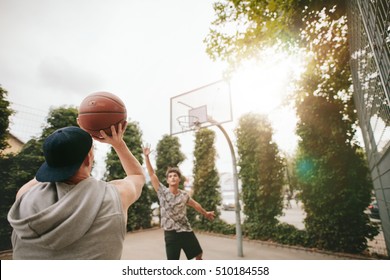 Streetball players on court playing basketball. Young guy taking shot to the basket with friend blocking. - Powered by Shutterstock