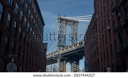 A street-level perspective looking down a cobblestone street in DUMBO, Brooklyn, featuring red brick buildings framing a view of the iconic Manhattan Bridge structure.Newyork