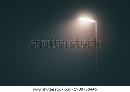 Streetlight post with bright light in a misty fog in the evening in a dramatic mood