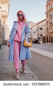 Streetstyle, Street Fashion Concept: Woman Wearing Trendy Sport Chic Style Outfit Walking In City. Blue Trench Coat, Sunglasses, Pink Hoodie, Trousers, Sneakers, Yellow Bag