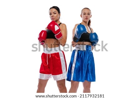 Strength, beauty and femininity. Two young beautiful girls, professional boxers in boxing shorts and gloves posing isolated on white studio background. Sport, competition, show, power, action concept.