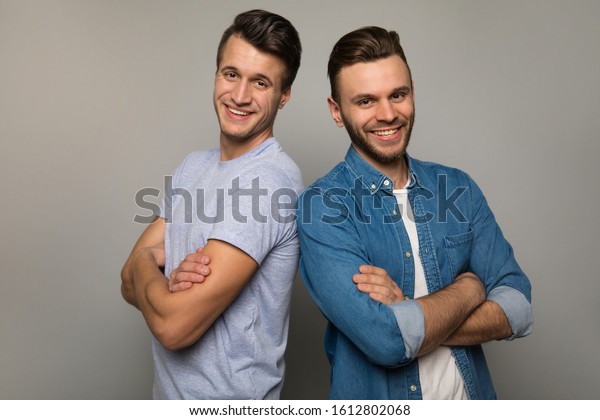 The strength of brothers.\
Two young men in casual clothes are standing back to back with\
cheerful facial expressions, posing with folded arms and smiling to\
the camera.