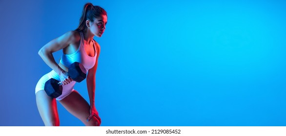 Strength training  Young sportive girl training and sports equipment isolated gradient blue  pink studio background in neon light  Modern sport  youth concept  Fitness  hobby  healthy lifestyle