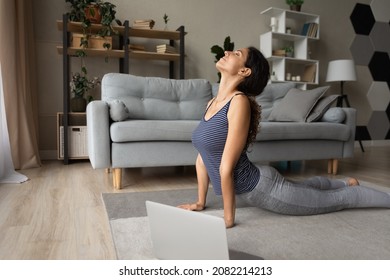 Strengthening muscles. Fit young hispanic woman do yoga exercises on floor before computer screen. Attractive millennial female practice cobra pose stretch shoulders and back reduce stress breath deep - Powered by Shutterstock