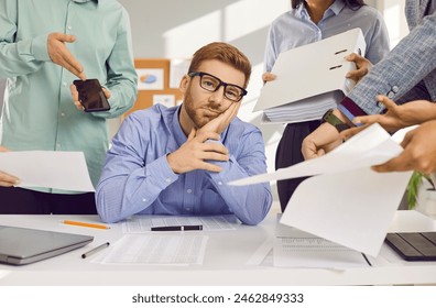 Stress, burnout and tired man sitting at the desk in office frustrated or overwhelmed by coworkers at workplace. Young businessman looking sad at camera. Overworked, multitasking concept. - Powered by Shutterstock