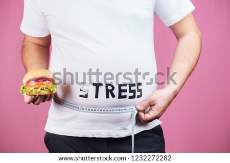 stress, eating problems, compulsive overeating, weight gain. overweight man with fresh appetizing burger and measuring tape