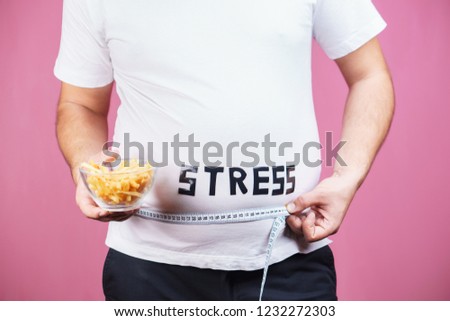 stress, eating problems, compulsive overeating, fat food, weight gain. overweight man with appetizing french fries and measuring tape
