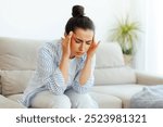 Stress, headache, illness. Upset mixed race woman sitting on a sofa in living room with eyes closed, suffering headache, vertigo, migraine, having cramp in a templess, need treatment and rest