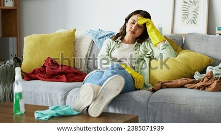 Stress, headache and woman with anxiety for laundry, clothes or overwhelmed by cleaning on sofa. Housework, depression migraine after washing, pile or chaos at home with vertigo or brain fog