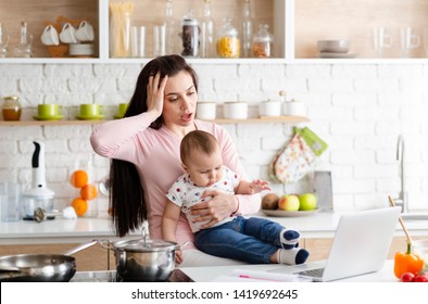 Stress Of Maternity Leave. Desperate Mother Looking At Laptop, Working With Baby In Kitchen At Home, Free Space