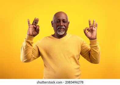 Stress Relief Concept. Edlerly African American Man Meditating With Closed Eyes, Keeping Calm On Orange Studio Background. Senior Black Male Practicing Yoga, Searching For Inner Balance