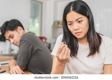 Stress, Unhappy Asian Young Couple Man, Woman Quarrel On Couch, Relationship In Trouble. Wife Holding Wedding Ring In Disappointment And Upset Her Husband, Which May Lead To Divorce. Problem Of Family