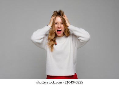 Stress. Woman Stressed Is Going Crazy Pulling Her Hair In Frustration And Shouting From Regret. Young Emotional Woman, Wears White Sweater, Standing Over Gray Background