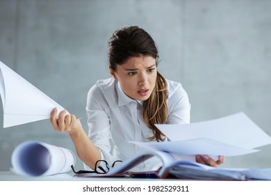 Stress At Work. Busy Female Architect Leaning On A Table And Looking At The Paperwork. There Are Blueprints On The Table. The Woman Has A Worried Expression And She Is Not Happy With A Project