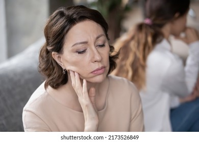 Stressed 60s mature woman feeling offended after quarrel with grown up daughter, ignoring each other, sitting on couch in silence. Unhappy different generations family having communication problems.