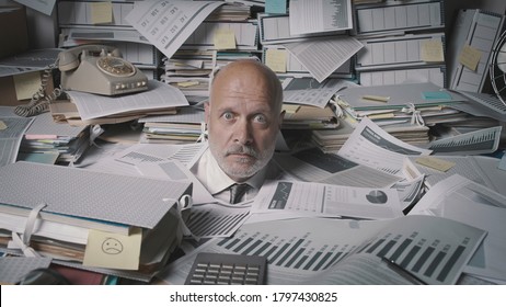 Stressed accountant working in the office, he is drowning under a lot of paperwork and overwhelmed by work