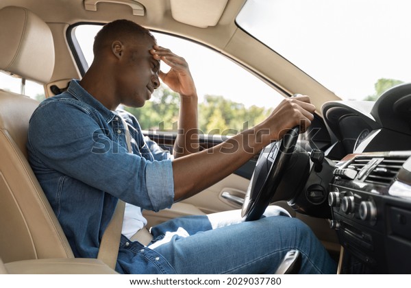 Stressed african american guy driver stuck in car\
traffic during rush hour, touching his head, getting late for\
meeting or flight, millennial black man going to airport by luxury\
auto, copy space