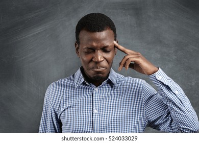 Stressed African Businessman With Painstaking Expression Struggling To Remember Something, Closing His Eyes Tight And Pressing Finger On His Temple As If Having Bad Headache. Short-term Memory Loss