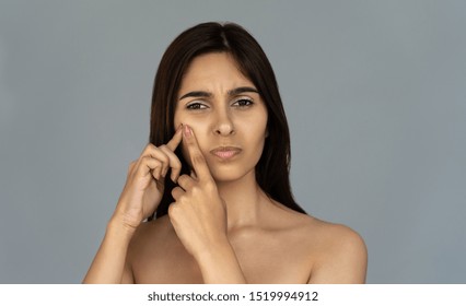 Stressed Annoyed Young Indian Woman Teen Girl Squeeze Remove Pimple Spot Worried About Face Skin Acne Problem Concept Look At Camera Isolated On Grey Studio Background, Cosmetology Facial Treatment