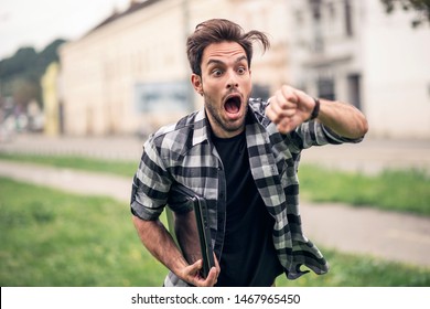 Stressed and anxious young man in a hurry, checking time and running, being late, holding his laptop in one hand - Shutterstock ID 1467965450