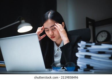 Stressed Asian Business Woman Working Late At Night In The Office Hands On Head Feeling Headache. Tired Woman Looking At Laptop Working Hard Sitting In The Dark Room Office. Overtime Concept