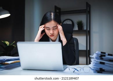 Stressed asian business woman working late at night in the office hands on head feeling headache. Tired woman looking at laptop working hard sitting in the dark room office. Overtime concept - Shutterstock ID 2121189407