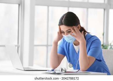 Stressed Asian doctor wearing medical mask while sitting at table in clinic - Powered by Shutterstock