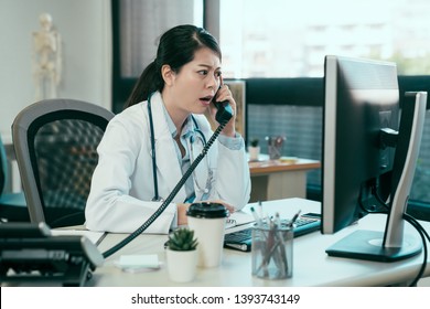 Stressed Asian Female Medical Worker Yelling While Speaking On Phone At Hospital Office. Angry Woman Doctor Argue With Annoyed Patient On Telephone. Mad Lady Nurse Having Conversation Bad Mood Clinic