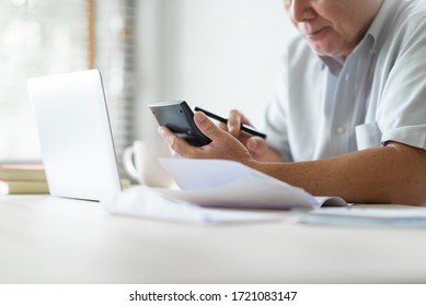 Stressed Asian Old Man Using Calculator For Calculate Family Budget, Monthly Expenses In Home During Economic Crisis. Senior Male Worry About His Debts With Bill, Passbook, Receipt And Laptop Computer