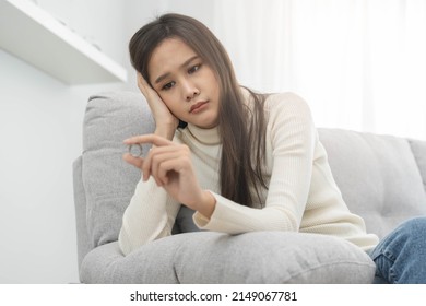 Stressed asian young couple, sad woman quarrel on couch, relationship in trouble. Wife's hand holding wedding ring in disappointment and upset her husband, which may lead to divorce. Problem of family